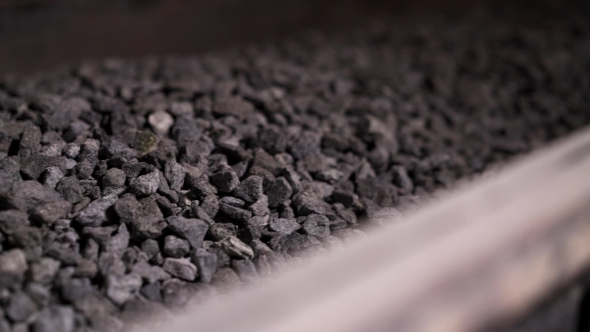 Close up of crashed stones transportation by conveyor to produce construction materials. Stock footage. Moving production line with macadam, industrial background.