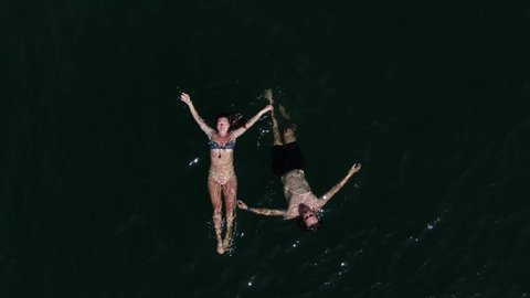 Instagram style drone shot showing a couple in love floating in Lake Havasu in the water during summer on an adventure traveling across the USA on a road trip. Warm inspiring shot flying up to reveal.