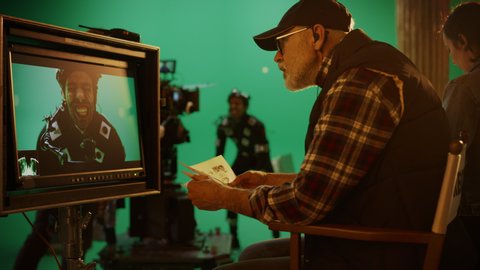 Director Looks at Display and Compares to Storyboard while Shooting Blockbuster Movie. Green Screen Scene with Actor Wearing Motion Caption Suit. On Film Studio Set Professional Crew Making Movie