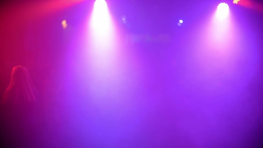 crowd of people dancing on the dance floor of a night club under the light of colored spotlights and lasers. Blurred silhouettes