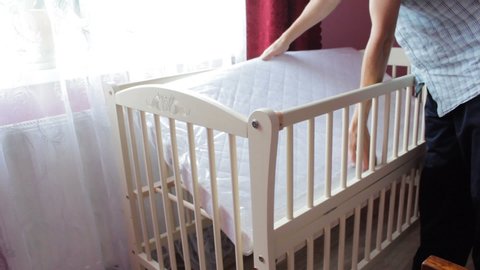 man puts the mattress in the cradle,the father folded the cradle for the baby and puts a new mattress