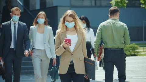 Blonde female emoloyer office manager businesswoman with face mask talking on smartphone walking home after work. Business district. Lockdown. Coronavirus. Self-isolation.
