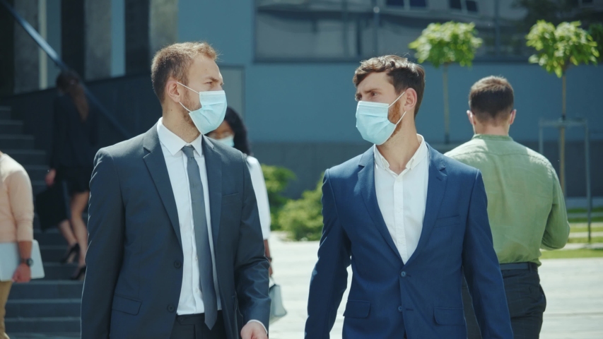 Couple of businessmen having corporate break outside office building. Two employees co-workers manager workers wearing protective face masks during lockdown. Royalty-Free Stock Footage #1054911338