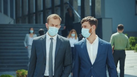Couple of businessmen having corporate break outside office building. Two employees co-workers manager workers wearing protective face masks during lockdown.