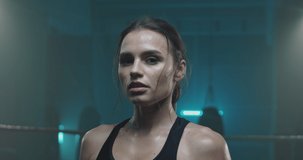Portrait of beautiful young tired and sweaty woman boxer turning face to camera with serious look at dark ring. Close up of pretty girl sportswoman looking at cam after physical training. - Powered by Shutterstock - Get 15% off with code: PIKWIZARD15