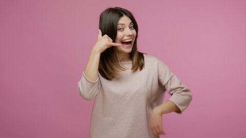 Hey you, let's contact by phone! Playful happy brunette pretty woman making telephone gesture near head and pointing to camera, offering communication. indoor studio shot isolated on pink background