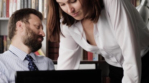 Sexual harassment concept. Male businessman manager working at computer, beautiful young woman comes to him and explains something, man examines woman with an appraising look. Close-up