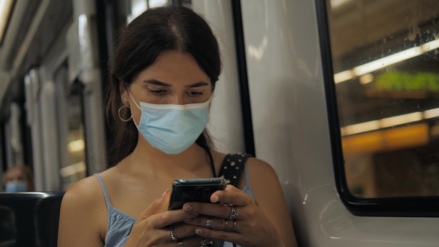 Coronavirus pandemic is over, quarantine end, young woman in protective medical face mask in a subway train using mobile. First tourists, open boarders, new reality after covid 19. Royalty-Free Stock Footage #1054915526