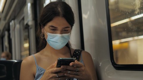 Coronavirus pandemic is over, quarantine end, young woman in protective medical face mask in a subway train using mobile. First tourists, open boarders, new reality after covid 19.
