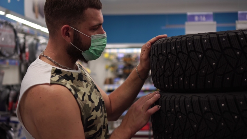 A man in a medical antiviral mask in a store chooses car tires.