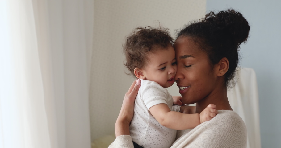 Head shot caring young african american mother lifting small kid daughter, comforting crying infant baby at home. Loving affectionate mixed race mum cuddling soothing little toddler child son. Royalty-Free Stock Footage #1054916519