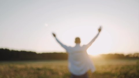 A caucasian man standing on the beautiful field during summer sunset, his hands are raised. A man look at the sky and pray. A man stand with his back to the camera. Defocusing Close up. SLOW MOTION