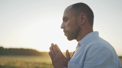 A caucasian man pray on the beautiful field during summer sunset.. A man's eyes are closed. Close up. SLOW MOTION