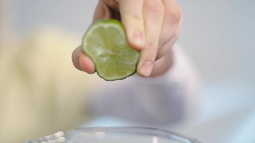 Woman hand squeeze fresh citrus lemon. Lemon juice drains from the pulp. Woman's hand squeeze half of green lime over the blender.