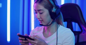 Young Asian woman gamer using smartphone and play in online video game. She playing online games with neon lights background.