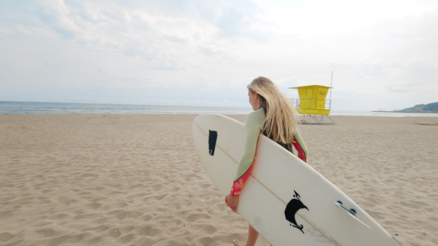 Slow motion shot of woman run to water with surfboard. Female surfer on sunny day at the beach laughing and smiling, happy to be outside and do physical activity to stay healthy and fit