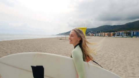 Slow motion shot of woman run to water with surfboard. Female surfer on sunny day at the beach laughing and smiling, happy to be outside and do physical activity to stay healthy and fit