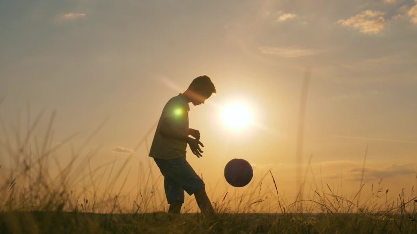 Happy boy with soccer ball. Kid dreams of sports. Silhouette of child in park with soccer ball. Happy child is dreaming with ball in park. Silhouette of boy in park. Happy boy with soccer ball