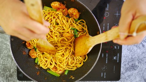 hand hold wooden turner stir-fried shrimp with small shallot onion, egg noodle,chinese mustard green in induction pan with smoke,red light indicator power on and fry menu button