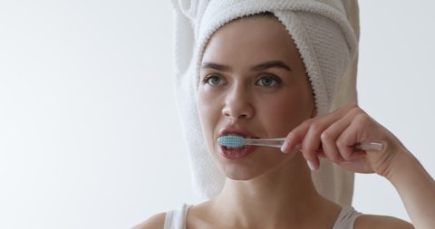 Oral Care Concept. Portrait of woman brushing her teeth, looking at mirror with towel on head