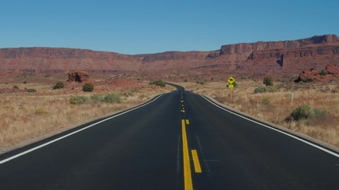 Motion on an empty road going into the distance to red mountain rocks in canyon landscape in the dried desert. The highway with black asphalt and orange markings. Slow motion, sunny day