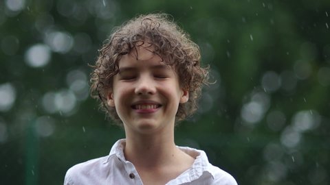 Close up portrait of cute young boy having fun catching rain drops. Happy childhood teenager in the pouring rain, wet season