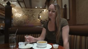 This video shows a young caucasian woman wearing glasses and eating delicious gumbo soup at restaurant.