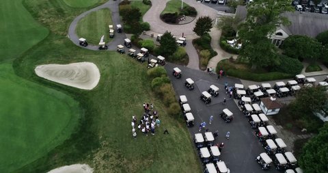 Drone video following a long row of golf carts driving along a concrete path before a golf tournament in Maryland