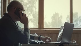 Side view of mature gray haired man talking emotionally on mobile phone pointing to the laptop screen. Online trader work at home - Powered by Shutterstock - Get 15% off with code: PIKWIZARD15