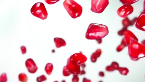 Juicy grains of ripe pomegranate are falling diagonally on the white background in slow motion