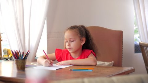Happy Little Girl or Cute primary child school child of 7-8 years old at home relaxing sits in house and paints on paper use colour pencils. Child draws,focused children elementary education concept.