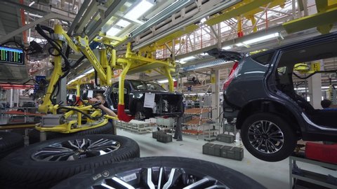 BELARUS, BORISOV - AUGUST 7, 2019: Automobile plant, modern production of cars, worker installs wheels on the car, workers at work, build process in automated production line.