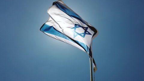 Flag of Israel waving in the wind, Sky and Sun Background. Intense Sunlight and flare, looking up a flag pole perspective.