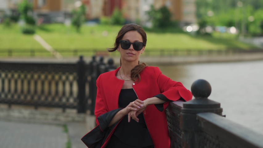 Pretty fashionable woman in red jacket is wearing sunglasses on the city street
