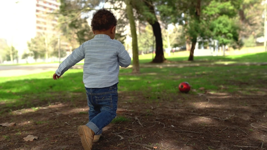 Little African American boy playing football with dad in park. Bald father running on lawn with little son and kicking ball. Family, summer and game concept