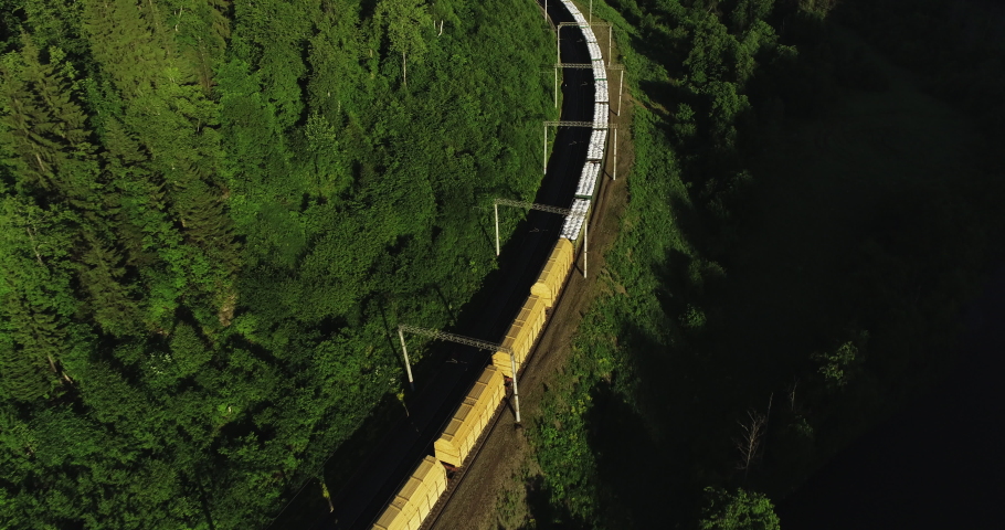 Freight train carries an electric locomotive by two-sided Trans Siberian railway near river in the forest Ural Mountains / Aerial Photography drone wide view at summer sunset  Royalty-Free Stock Footage #1054955969