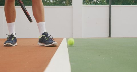 Low section of a Caucasian man wearing tennis whites spending time on a court, playing tennis on a sunny day, holding tennis racket, bouncing a tennis ball, in slow motion.