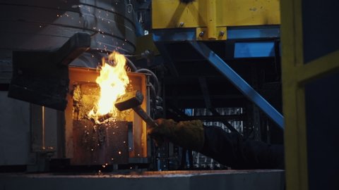 Factory worker hand uses hammer to drum the metal nail into the furnace, oven. metal cast, foundry, steel production plant, close up, slow motion