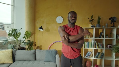 Professional black sportsman exercising aerobics doing shoulder and arm stretches warming-up before workout. Indoors. Apartment. Fitness. Sports activity. - Βίντεο στοκ