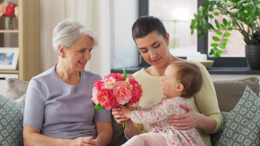 Family, generation and celebration concept - mother with baby daughter giving grandmother flowers at home