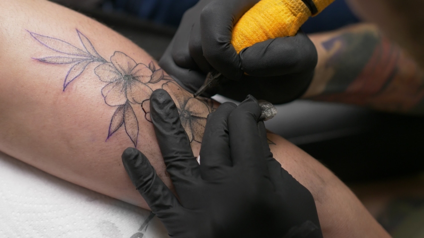 Close-up of a tattoo artist makes a tattoo on a woman's arm. Professional tattooist works in studio. Close-up view of female hand making tattoo. 4K. High quality 4k footage Royalty-Free Stock Footage #1054973951