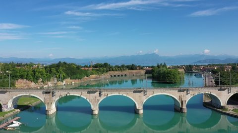 Frecciarossa high-speed train passes an arched railway bridge over a river in the background Lake Garda Italy. Red high-speed train on the bridge