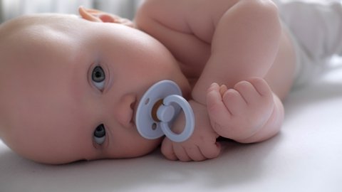 Adorable cute naked toddler suck pacifier relaxing lying on bed feeling calmness enjoying happy childhood close up attractive baby resting looking at camera