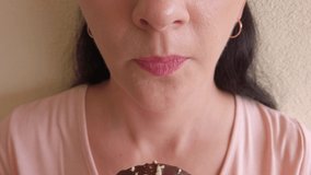 fair-skinned young woman with long dark hair eats donut with brown chocolate icing. Portrait. Close-up. Selective focus video. 4k
