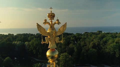 Petersburg / Russia - 06.20.2019 : Peterhof Petrodvorets golden three-headed eagle top symbol royal old imperial palace. Historical suburb landmark. Seagull flies and sits on top. Fountain. Aerial