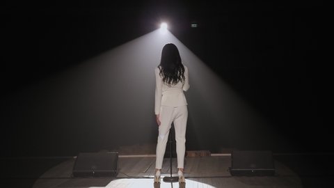 The silhouette of the singer in the dark on the stage under the light of a single white bright spotlight, the light is turned off and the stage is plunged into darkness. Slow motion.
