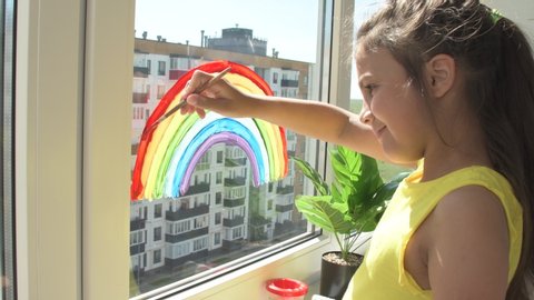 Girl painting rainbow on window during quarantine at home. Thank You Essential Workers message concept.
