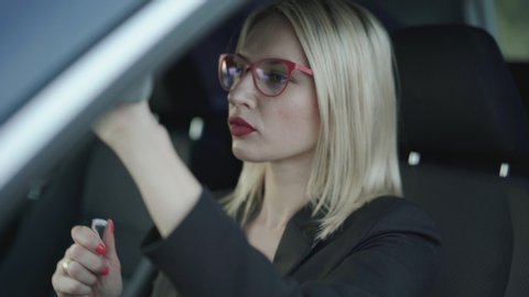 Glamorous blonde in glasses applying the red pomade at mirror in car. 4K
