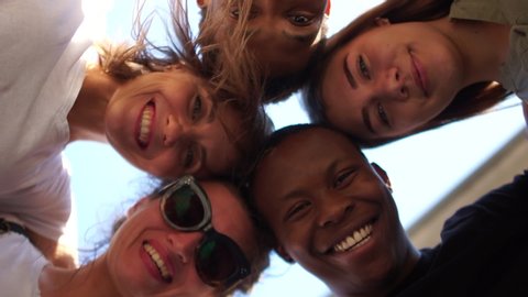 Close portrait of five young students, tolerance and no racism concept. Interracial group of students leaned over the camera against the sky