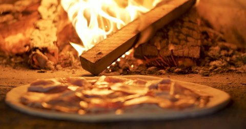 Close Up of Placing Pizza in Woodfired Pizza Oven, using Pizza Peel. Close up of Appetizing Pizza with Spices, Herbs, Fresh Vegetables, Tomato Sauce. Appetizing Dish. Traditional Italian Food.